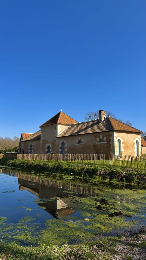 Historic stone building with terracotta roof reflected in pond at Cloffy B&B, Nouans-les-Fontaines, France