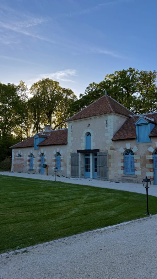 Cloffy cottage exterior in Nouans-les-Fontaines with blue shutters, stone facade, manicured lawn at dusk