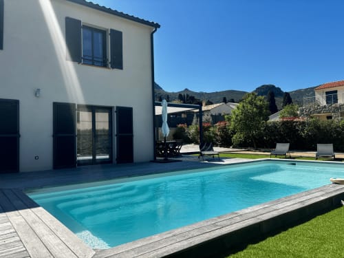 Private villa with turquoise swimming pool, wooden terrace, loungers, and mountain views in Zilia, France