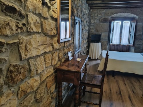 Rustic stone hotel room at Posada La Colodra with wooden desk, chair, bed, and arched windows