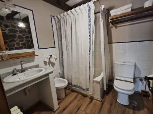 Bathroom at Posada La Colodra with sink, toilet, shower with white curtain, and wood flooring