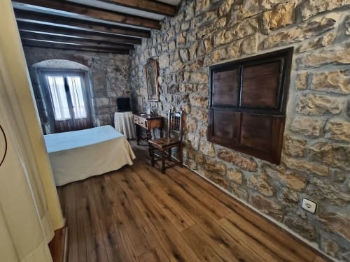 Rustic stone bedroom at Posada La Colodra with wooden floors, TV, and traditional furnishings