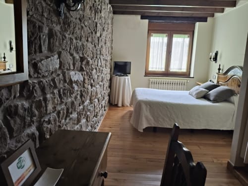 Cozy double bedroom at Posada La Colodra with rustic stone wall, wooden beams, and mountain views from windows
