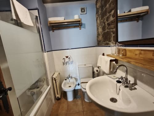 Bathroom at Posada La Colodra with sink, toilet, shower, and wooden shelving in Spain