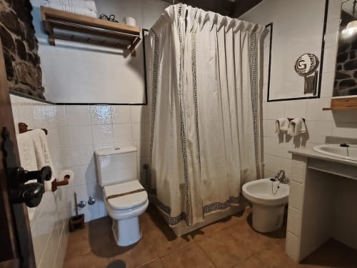 Bathroom at Posada La Colodra hotel with toilet, sink, shower with patterned curtain, towel rack, and white tile walls
