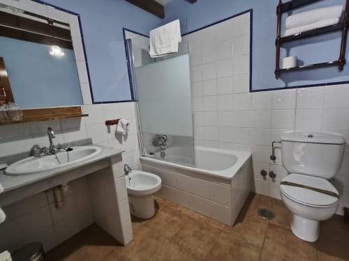 Bright bathroom at Posada La Colodra hotel with bathtub, sink, toilet, and white tile walls