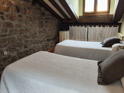 Rustic double room with two beds at Posada La Colodra, Spain, featuring exposed stone walls and wooden beams