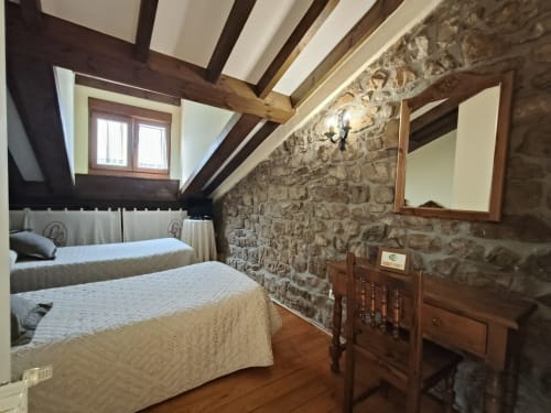 Rustic double bedroom at Posada La Colodra with exposed stone walls, wooden beams, two beds, and mountain views through