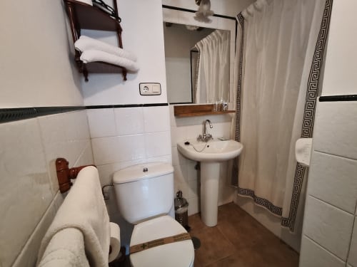 Bathroom at Posada La Colodra hotel featuring white tiled walls, pedestal sink, toilet, and shower with decorative border