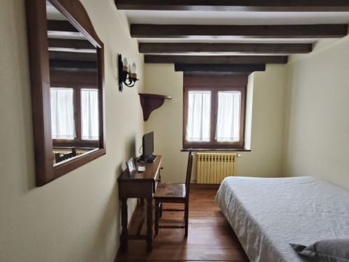 Bright single room at Posada La Colodra with wooden beams, desk with TV, radiator, and mountain views from windows