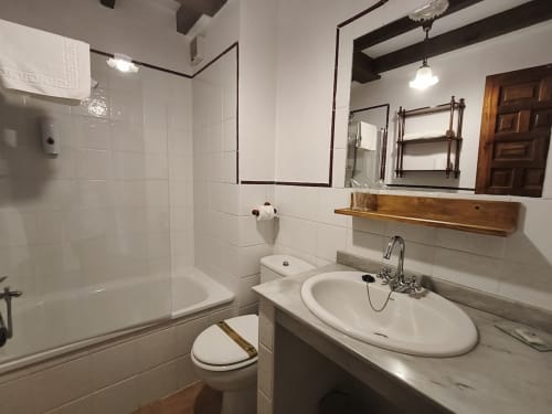Clean bathroom at Posada La Colodra hotel with white tiles, sink, toilet, and glass shower enclosure