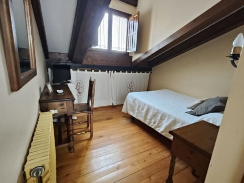 Posada La Colodra single room with wooden beams, bed, desk, and mountain views through high window
