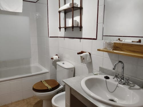 Clean bathroom in Posada La Colodra with white sink, toilet with wooden seat, shower, and mirror