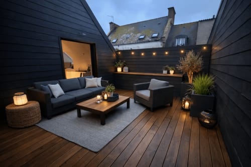 Cour élégante en soirée au Hangar 7 à Guilvinec, France, avec terrasse en bois foncé, sièges confortables et ambiance chaleureuse