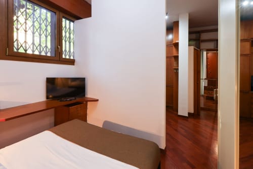 Camera da letto moderna a Solumnia Milano con letto, scrivania in legno, TV e pavimenti in parquet