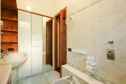 Bagno moderno nello studio Urban Nest dell'hotel Milano, con doccia in vetro, lavabo bianco e mensole accent in terracotta
