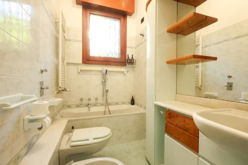 Bagno moderno nello studio Solumnia di Milano con piastrelle bianche, ripiani in legno, doccia in vetro e wc
