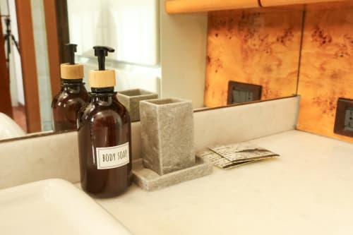 Amenità bagno presso Solumnia Milano: dispenser di sapone marrone, saponetta naturale e articoli da toilette in omaggio su bancone in marmo