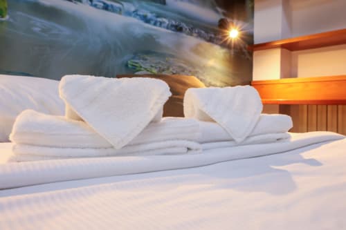 Asciugamani bianchi ordinatamente piegati e asciugamani a forma di cuore sul letto dell'hotel Solumnia a Milano