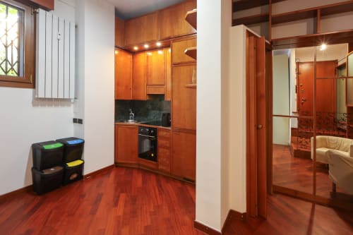 Moderno monolocale a Milano con pavimento in legno rosso, cucina attrezzata e armadi a specchio