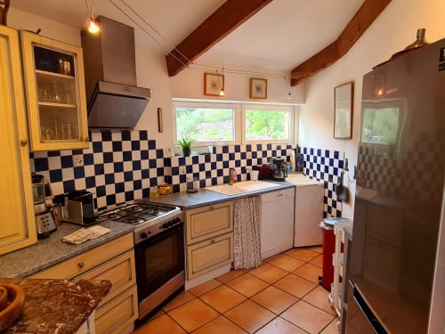Charming kitchen with blue and white checkered backsplash, wooden beams, and terracotta tiles at Domaine de L'Échappée Belle