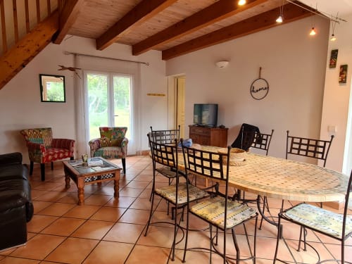 Spacious open-plan living and dining area at Domaine de L'Échappée Belle with terracotta tiles, wooden beams, and garden