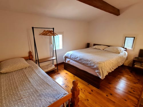 Bright bedroom at Domaine de L'Échappée Belle with two beds, wooden floors, exposed beam, and windows.