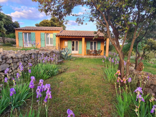 Charming orange cottage with green shutters surrounded by purple irises at Domaine de L'Échappée Belle in Entrecasteaux,