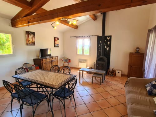 Spacious open-plan living area at Domaine de L'Échappée Belle with dining table, fireplace, and exposed wooden beams