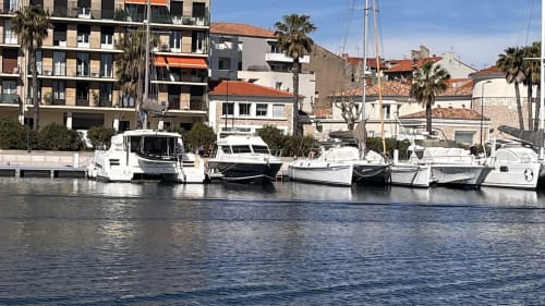 Bateaux blancs amarrés au front de mer à Sète avec des bâtiments méditerranéens et des palmiers en arrière-plan