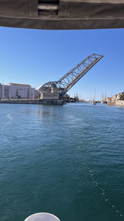 Pont-levis surélevé au-dessus d'une voie navigable turquoise avec voiliers et bâtiments portuaires dans une ville méditerranéenne