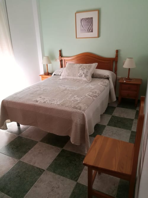 Double bedroom at Hostal San Andres in Carboneras with wooden bed, beige bedding, mint walls, and checkered tile floor