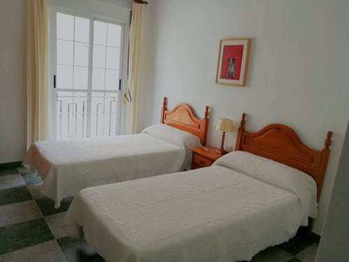 Twin bedroom at Hostal San Andres in Carboneras with wooden beds, white linens, and balcony access