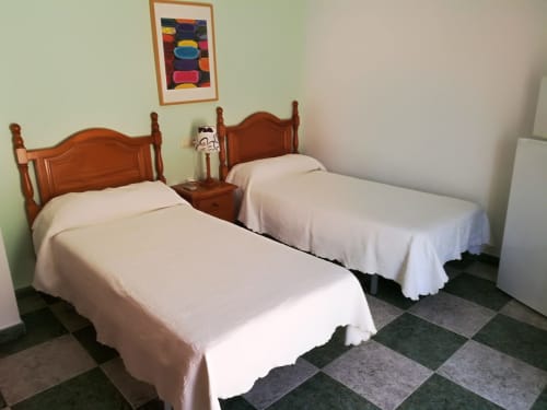 Twin bedroom at Hostal San Andres in Carboneras with wooden beds, white linens, and checkered tile floor