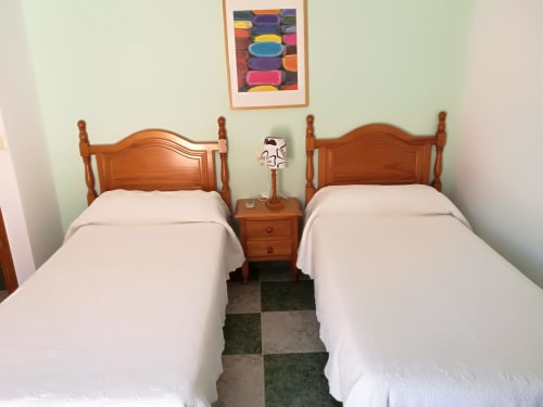 Twin bedroom at Hostal San Andres in Carboneras with wooden beds, bedside table, and colorful artwork on pale green walls
