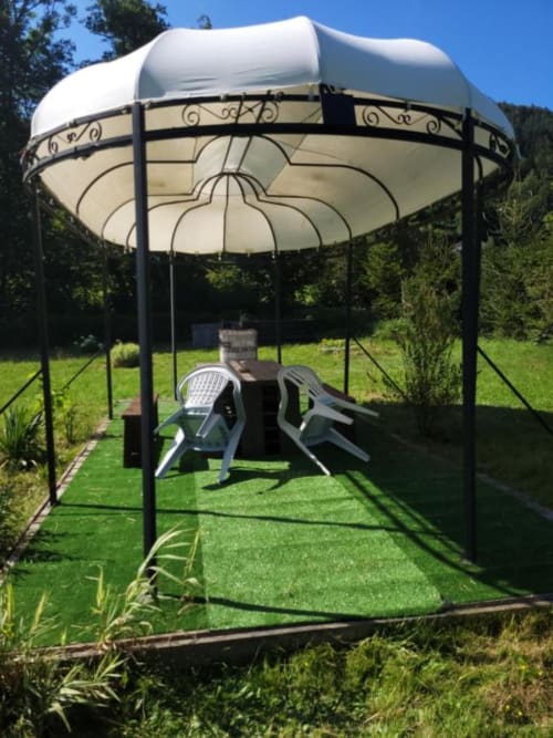 Élégante pergola métallique aux voiles crème et structure noire décorée dans le jardin verdoyant des Gîtes les Grandes voies, Le Ménil
