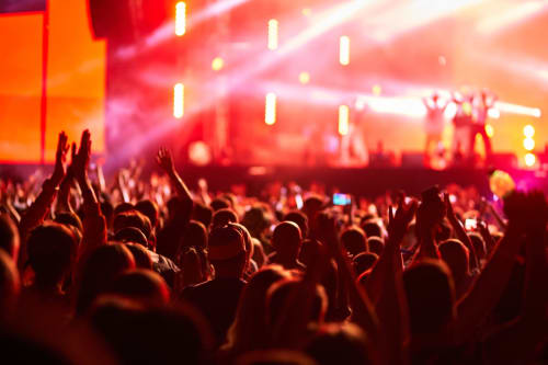 Foule de concert avec les mains levées sous des lumières de scène rouges vibrantes et des faisceaux néon