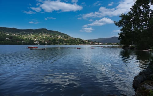 Vue pittoresque du lac aux Gîtes et chalet les Grandes voies au Ménil, avec montagnes, collines boisées et barques amarrées