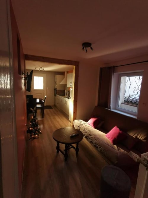 Salon cozy des Gîtes les Grandes voies au Ménil avec canapé beige, foyer et cuisine ouverte