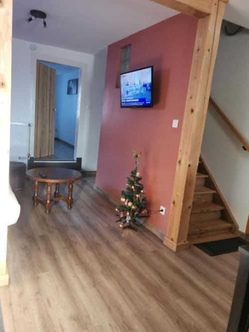 Salon des Gîtes les Grandes voies avec mur d'accent corail, TV, poutres en bois, petit sapin de Noël et accès à la chambre bleue