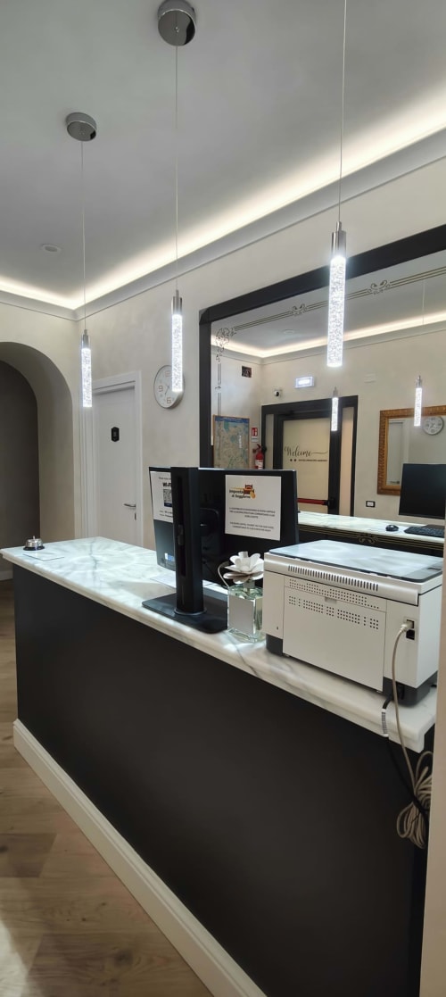Moderno banco ricezione dell'Hotel Principe Amedeo Roma con piano in marmo, lampade a sospensione e terminali informatici