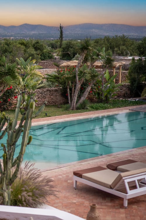 Piscine turquoise du Domaine Belhazar à Essaouira avec transats, paysage désertique et Atlas en arrière-plan