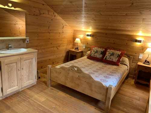 Wooden chalet bedroom at Chez Francine with queen bed, ensuite bathroom, and warm lighting in Notre Dame de Bellecombe