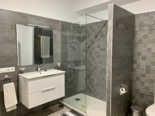 Modernes Badezimmer mit weißem Waschtisch, grauem Fliesenbelag, gläserner Duschkabine und WC im Apartment Salud Vacacional 2, Santa
