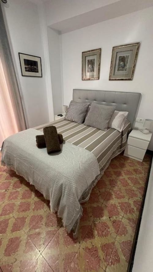 Modernes Schlafzimmer mit grauem Kopfteil, gestreifter Bettwäsche, Wandgemälde und Terrakottafliesen in Santa-Cruz-Apartment