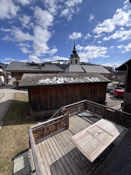 Wooden balcony overlooking alpine village with traditional chalets and church steeple, Notre Dame de Bellecombe