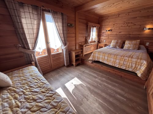 Spacious wooden chalet bedroom with multiple beds, plaid bedding, and garden views at Chez Francine, Notre Dame de Bellecombe