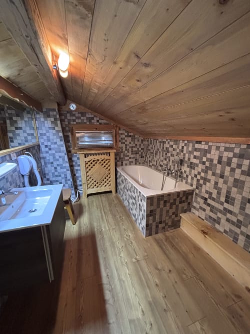 Spacious bathroom in Chalet Marie Claire with wooden ceiling, checkered tile walls, bathtub, sink, and heated amenities at