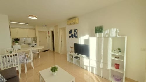 Modern apartment living room with TV, white storage, dining area, kitchen, and ocean view in Santa Cruz de Tenerife