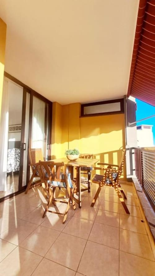 Sunny outdoor terrace with wooden dining furniture, yellow awning, and sea view at Olivia Playa La Arena apartment, Tenerife